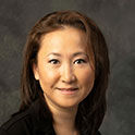 Cha is pictured from the neck up. She has tan skin, dark brown hair and is smiling. 