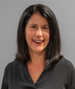 a woman in a dark shirt with brown shoulder length hair smiling