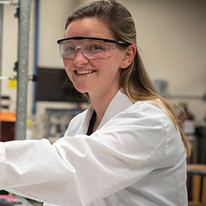 female student wearing a lab cat and protective eye wear in a lab